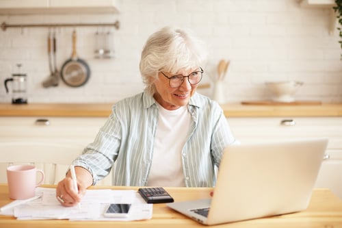 concepto-personas-edad-tecnologia-ocupacion-imagen-interior-atractiva-mujer-jubilada-pelo-gris-sonriente-usando-computadora-portatil-trabajo-remoto-sentada-cocina-papeles-ganando-dinero-linea