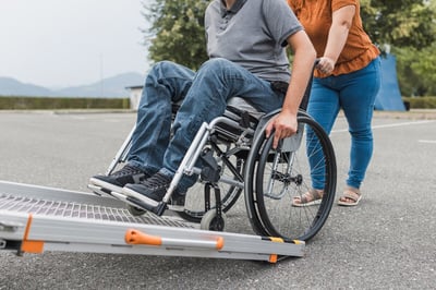 female-assistant-pushing-man-with-disability-wheelchair-user-up-car-ramp-into-van