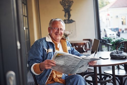 stylish-senior-in-fashionable-clothes-and-in-glasses-sits-in-the-cafe-and-reads-newspaper